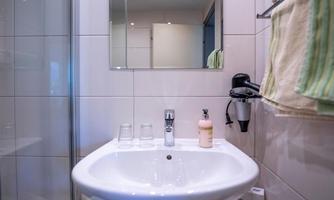 A modern bathroom with a sink, mirror, and hygiene items. Towels hang on the wall, and there are glasses on the sink.