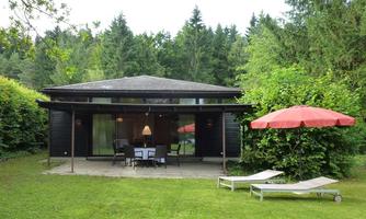 A modern house in a green garden with a terrace .. In the foreground, there are two loungers on the lawn.
