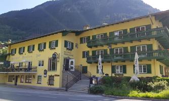 A yellow hotel with green balconies and terraces. In the background, mountains rise under a clear sky.