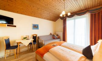 A cozy hotel room with two beds and a wooden ceiling. A table and chairs are available, as well as a large window view.