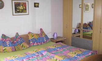 A cozy bedroom with a colorful bedding set and pillows. In the background, there is a mirror and decorative pictures on the wall.