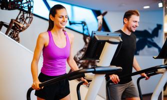 Two people are training in a modern gym on cross trainers. The woman is wearing a purple shirt and the man a black shirt.