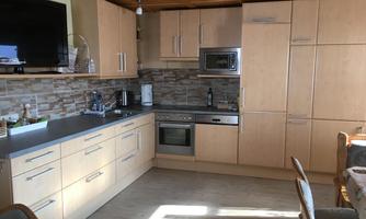 A modern kitchen with light wooden cabinets and stainless steel appliances. The room has plenty of natural light and a cozy dining area.