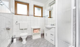 A modern bathroom with white tiles and windows. It includes a shower, a sink, and a toilet.