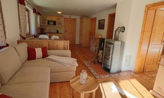 A cozy living room with a beige sofa and a small wooden table. The room has wooden floors and a warm, inviting atmosphere.