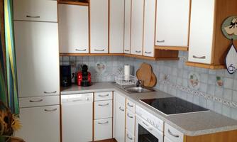 A modern kitchen with white cabinets and a bright, friendly design. The equipment includes a cooktop, an oven, and various kitchen appliances.