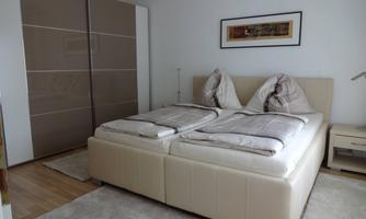 A modern bedroom with a large double bed and an elegant dresser. A piece of artwork hangs on the wall and the floor is covered with a carpet.