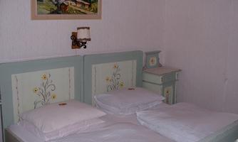 A cozy bedroom with a double bed and a light color scheme. A picture of mountains and a house hangs on the wall.