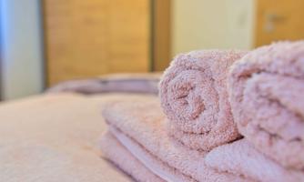 A quiet room with freshly washed, pink towels on a bed. In the background, a wooden cupboard can be seen.