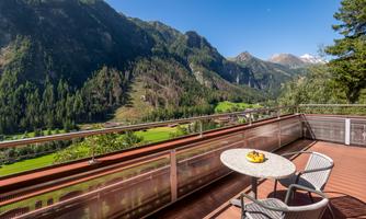 A beautiful balcony with a view of green valleys and majestic mountains. A fruit bowl is on the table and the sun is shining.