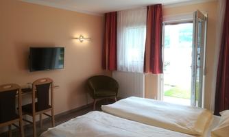 A cozy room with two beds and a television. Large windows provide plenty of daylight and a view of the outside.