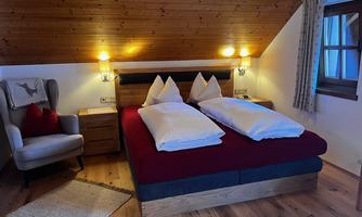 A cozy bedroom with a large bed and red bedcovers. An armchair and a rug complement the warm atmosphere of the room.