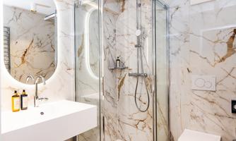 A modern bathroom with marble walls and a glass shower. The vanity area is designed simply and elegantly.