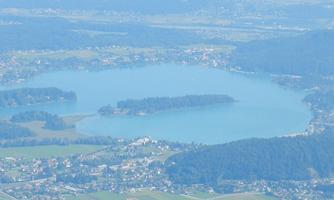 A beautiful view of a lake surrounded by green forests and small villages. The calm surface of the water reflects the landscape.