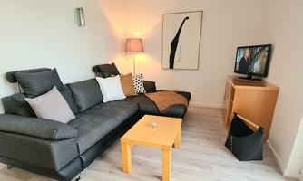 A modern living room with a gray couch, a wooden table, and a television. There is a lamp and a picture on the wall that makes the room cozy.