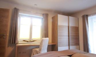 A cozy bedroom with a window and a workspace. The room is bright and modernly furnished.