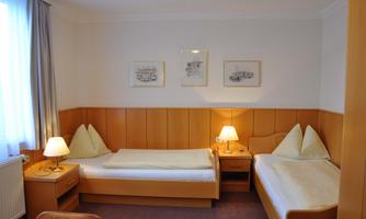 A simple room with two beds and warm wooden details. There is a lamp and artworks on the wall.