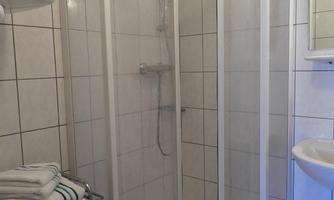 A modern shower with glass doors and white tiles. Towels are neatly arranged on a rack beside it.