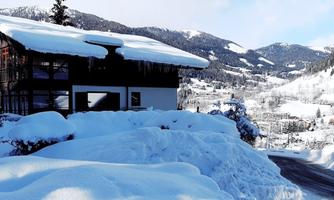 A cozy house in the snow with a picturesque mountain landscape in the background. The surroundings are wintry and peaceful.