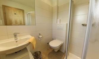 A modern bathroom with a shower, sink, and toilet. The walls are brightly tiled, and the room looks clean and tidy.