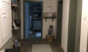 A bright hallway with wooden floor and white walls. On the left side are shelves and on the right side are several doors.