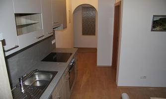 A modern kitchen with cabinets in bright colors and a stove. In the background, a hallway with an arch can be seen.