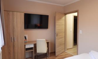 A modern room with a television on the wall and a desk. The walls are painted in soft colors and the door leads to another room.