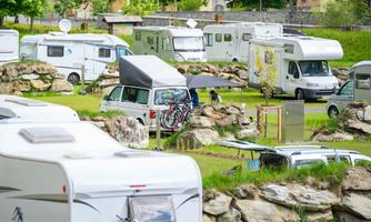 A campsite with several motorhomes and caravans, surrounded by green grass and rocks. The atmosphere is relaxed and inviting.