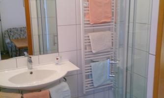 A modern bathroom with a shower and sink. Towels in soft colors hang on a towel rack.