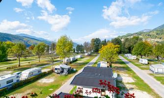 A campsite with caravans and beautifully designed pitches. The surroundings are green and offer a nice view of the mountains and the sky.