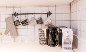 A modern kitchen with cups hanging from a rack, and various kitchen appliances. On the countertop, there is a kettle and a coffee maker.