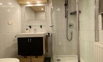 A modern bathroom with a semicircular shower. It has bright walls, a wooden ceiling, and a sink with a black base cabinet.