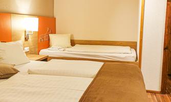 A simple bedroom with two single beds and a warm color tone. The walls are kept neutral and there is a bedside lamp next to the bed.