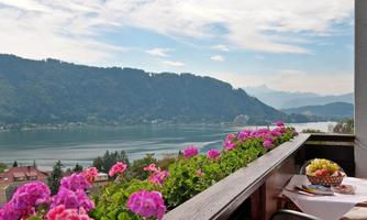 A beautiful view of a lake, surrounded by mountains. Colorful flowers adorn the balcony in the foreground.