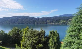 A quiet lake surrounded by green trees and gentle hills. The sky is clear and the landscape radiates peace.