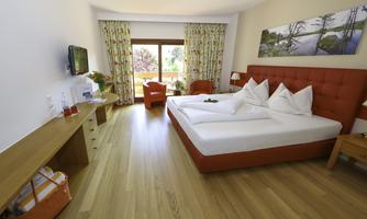 A modern hotel room with a red bed and two red chairs. Large windows let in plenty of daylight and offer a view outside.