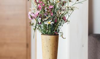 A beautiful bouquet of flowers in a stylish vase is standing on a table. Next to it, a book lies on the wooden surface.