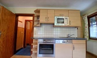 A modern kitchen with light wood cabinets and a stainless steel sink. The amenities include an oven, a cooktop, and a microwave.
