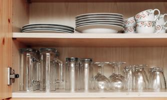 A cupboard with glasses, plates, and cups is visible. The shelves are tidy and well-organized.