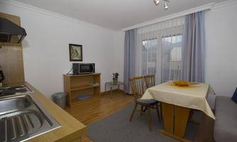 A cozy kitchen area with a table and chairs. Large windows provide plenty of daylight.