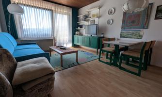 A bright and inviting living space with a blue sofa and a wooden table. A large window area provides plenty of daylight.