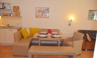A cozy dining area with a table and chairs, decorated with dishes and a flower. The modern kitchen is visible in the background.