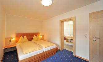 A cozy bedroom with two beds and yellow pillows. The room is bright and provides access to a bathroom.