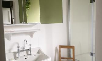 A bathroom with a sink and a chair. The walls are painted green and there is a shower cubicle.