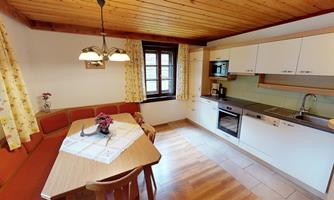 A bright kitchen with wooden ceilings and a dining area. The modern amenities include a stove, a refrigerator, and windows with curtains.