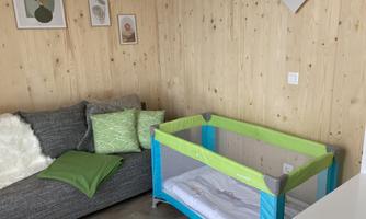 A cozy room with a gray sofa and a green children's bed. Some pictures hang on the walls, and the wood paneling adds warmth to the room.