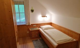 A cozy bedroom with wood paneling and a single bed. The window lets in plenty of natural light, and the quiet atmosphere invites relaxation.