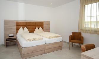 A modern bedroom with a double bed and two pillows. There is a cozy armchair and plenty of natural light coming through the window.