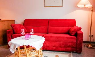 A red sofa with cushions in a cozy room. There is also a round table with glasses and a lamp in the background.