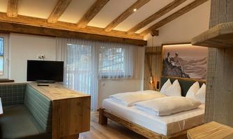 A cozy room with wooden ceilings and a large bed. There is a dining table and a television, as well as plenty of natural light through the windows.